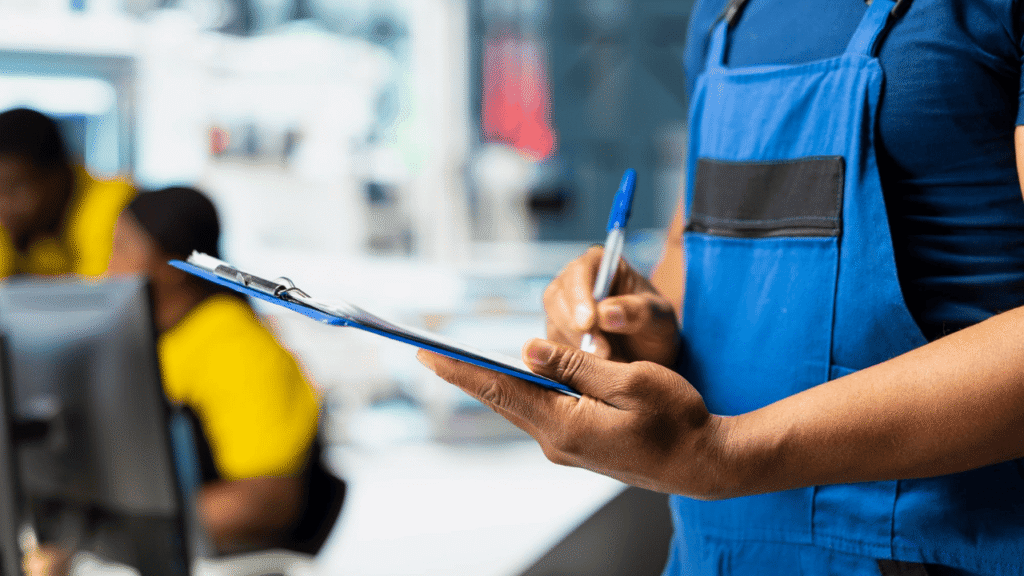 Fleet staff member reviewing and writing on a clipboard, performing a logbook auditing service while another employee works in the background.